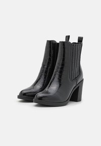 Bottines noires à la cheville avec une finition brillante à texture crocodile, panneaux latéraux élastiques et un talon haut épais. Bout arrondi.