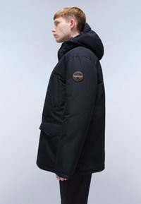 Svart isolerad jacka med huva, med en tonad patch på vänster ärm, framfickor och en elegant, rak design.
