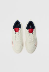White sneakers with a smooth texture, featuring red and navy accents, round toe, and stitched details along the sides.