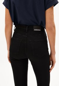 Jeans negros de talle alto con una textura suave, que cuentan con dos bolsillos traseros y una etiqueta de marca en la pretina.