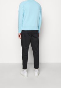 Sudadera azul claro con mangas raglán y puños acanalados, combinada con pantalones negros ajustados y zapatillas blancas, vista desde atrás.