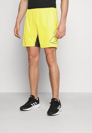 Pantaloncini sportivi giallo brillante con accenti neri e motivo geometrico, dotati di fascia elastica in vita e aperture laterali per la mobilità.