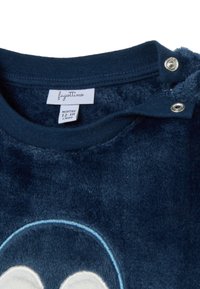 Marineblauwe fleece kledingstuk met ronde hals, voorzien van drukknoopsluitingen en een zachte textuur. Etiket toont maat: 12-18 maanden, merk: Fagottino.