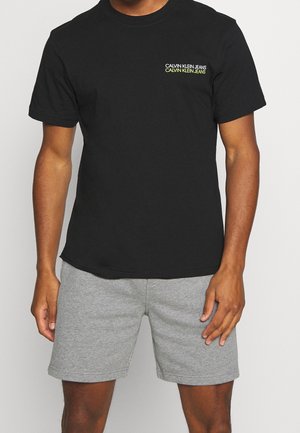 Czarna bawełniana koszulka z krótkim rękawem, z żółtym haftowanym napisem logo po lewej stronie. W zestawie z szarymi szortami.