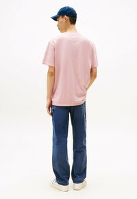 Lichtroze t-shirt met korte mouwen, relaxte pasvorm, verbonden met blauwe spijkerbroeken en witte sneakers. De achterkant toont een eenvoudige halslijn en een casual ontwerp.