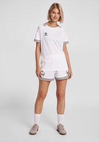 White athletic jersey with gray accents, featuring a round neckline and short sleeves. Paired with matching white shorts and sporty shoes.