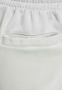 Pantalones de chándal gris claro en primer plano que presentan un bolsillo externo, una cinturilla fruncida y una suave tela de algodón texturizada.