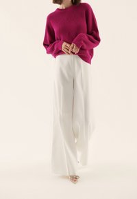 Sweter dziany w kolorze fuksji z prążkowaną fakturą, zestawiony z białymi szerokimi spodniami. Spodnie mają gładkie wykończenie, uzupełnione sandałami na paski.