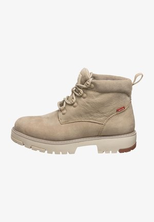 Bottines en cuir beige avec une finition texturée, bout rond et semelle blanche robuste. Présente un système de laçage et une petite languette à l'arrière.