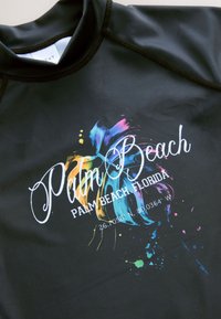 Juodas apsauginis marškinėlis su spalvingu purslo dizainu, ant kurio užrašyta „Palm Beach“ ir koordinatės, pabrėžiantys ryškias mėlynos, rožinės ir geltonos spalvų atspalvius.