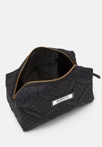 Bolsa de tela negra acolchada con un zipper dorado, que cuenta con un bolsillo interior y una etiqueta en un costado. El diseño tiene un patrón texturizado.