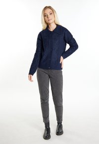Marineblå stickad cardigan med en strukturmönstrad diamantdesign, knäppning fram med knappar och stor krage. Para ihop med grå byxor och svarta ankelstövlar.