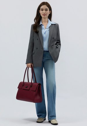 Grauer doppelt geknöpfter Blazer über einem hellblauen Hemd, kombiniert mit ausgestellten hellen Jeans. Eine burgunderfarbene strukturierte Handtasche mit zwei Tragegriffen.