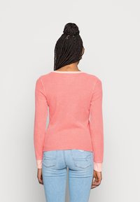 Långärmad ribbad topp i korallrosa. Mjuk textur med rund halsringning och kontrasterande manschetter. Fitted design med en lätt kurva vid nederkanten.