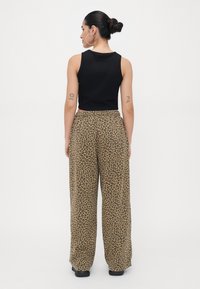 Zwarte mouwloze top gecombineerd met wijde, beige en bruine broek met panterprint. Heeft een hoge taille en een ontspannen pasvorm.