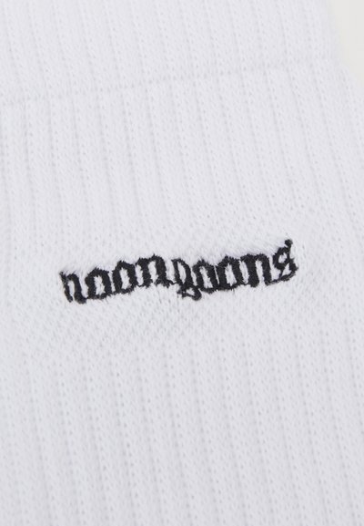 Chaussette blanche à côtes avec un texte brodé noir indiquant "haomganga." Le matériau semble doux avec une texture respirante.