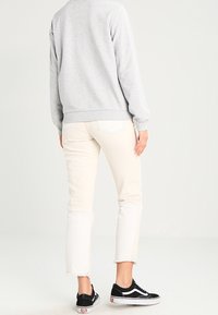 Felpa grigia chiara abbinata a jeans cream tagliati con orli sfrangiati, indossati con sneakers nere. Outfit casual visto da dietro.
