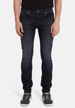 Donkerblauwe denim jeans met een slim fit, knoopsluiting, vijf zakken en subtiele wassingdetails. Gecombineerd met zwarte sneakers, wat een gelaagde textuur toont.