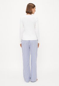 Vit långärmad tröja ihop med blå och vita rutiga pyjamasbyxor. Byxorna har vida ben och ett rutigt mönster, med en slät tygtextur.