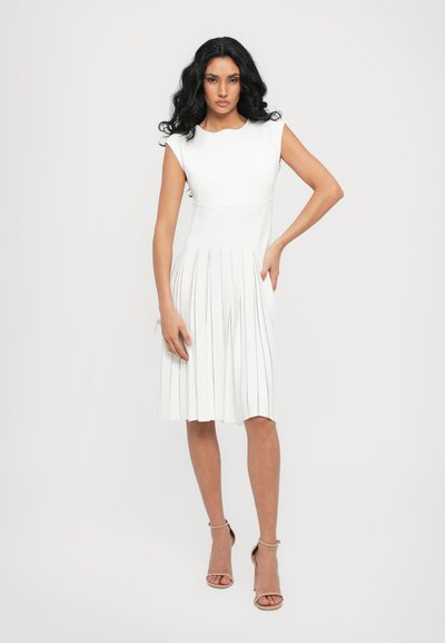 White dress with a fitted bodice and pleated skirt featuring vertical stripes. Smooth texture and round neckline, paired with beige heels.