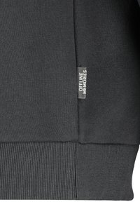 Schwarzes Sweatshirt mit gerippten Bündchen und Saum, aus einem strukturierten Stoff gefertigt und mit einem kleinen Etikett, auf dem "OFFLINE MEMORIES" sicher an der Seite genäht ist.