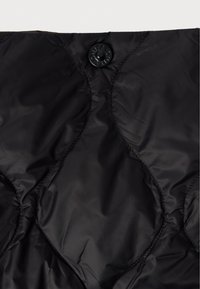 Μαύρο επενδεδυμένο υλικό με γυαλιστερή φινίρισμα, με κυκλικό κούμπωμα και διαμαντοειδή σχέδια ραφής.