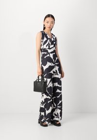 Mono floral en blanco y negro, con cuello de cisne, diseño de pierna ancha y cintura ajustada. Combinado con un pequeño bolso negro.
