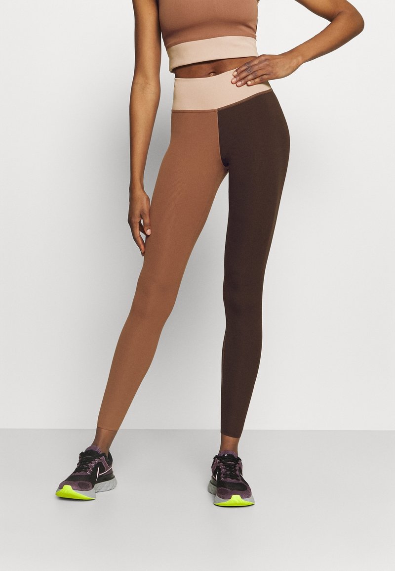 High-waisted leggings in brown tones with a color-blocked design. Soft, stretchy material with a smooth texture, paired with black shoes.