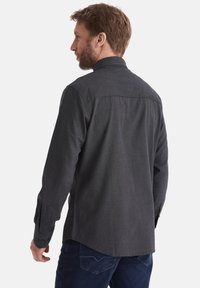 Dunkelgraues Langarmhemd aus strukturiertem Stoff mit Knopfmanschetten und abgerundetem Saum, von hinten an einem männlichen Modell gezeigt.