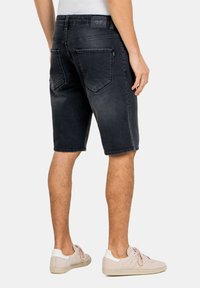 Shorts de mezclilla negra con una textura desgastada, con dos bolsillos traseros y un dobladillo recto. Llevados con zapatos de color claro.