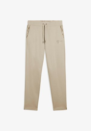 Pantaloni sportivi beige con vita elastica e cordino regolabile. Le tasche laterali presentano un bordo decorato. Logo sottile sul davanti.