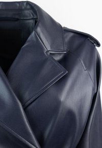 Cappotto in pelle blu navy con una texture liscia, caratterizzato da ampi revers, spalline e un design minimalista.