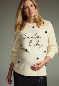 Kremasti pulover s crnim pomponima i izvezom "Santa Baby". Nosi se uz crnu suknju sa šljokicama, sa rebrastim manžetama i rubom.
