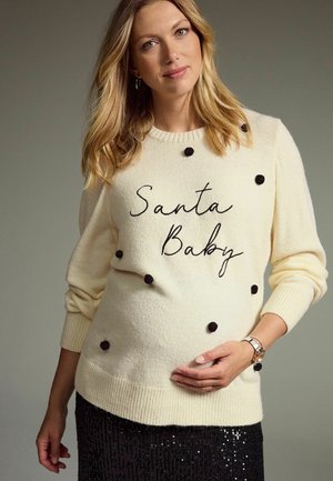 Cream-colored sweater with black bobble accents and embroidered "Santa Baby." Worn over a black sequin skirt, with ribbed cuffs and hem.