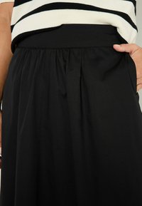 Falda negra con un diseño fruncido, que presenta una cintura suave. El material parece suave y ligero, adecuado para un uso informal o formal.