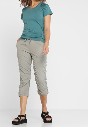 Woman wearing teal short-sleeve top, light gray cropped pants with drawstring, and black platform sandals standing against a plain background.