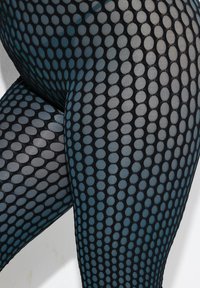 Zwarte mesh legging met een groot circulair patroon in verschillende tinten blauw. De stof is doorschijnend, waardoor de huid eronder zichtbaar is.