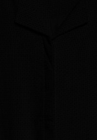 Chemise noire à manches longues avec un motif discret de petits points sur l'ensemble et un col classique pointu.