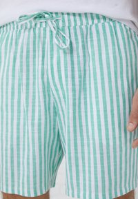 Lightweight, striped shorts featuring alternating green and white vertical stripes. Drawstring waistband and soft, textured fabric.