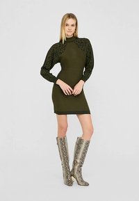Vestido de punto verde oliva con cuello alto y mangas con estampado de leopardo. Combinado con botas metálicas hasta la rodilla con estampado de serpiente. Textura suave.