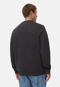 Zwarte crewneck sweater met een textuur bovenpaneel, geribbelde boorden en zoom; gedragen met lichtblauwe, losse spijkerbroek. Achteraanzicht.
