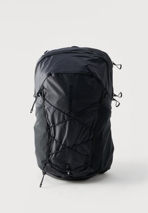 Zaino Salomon nero con cordini elastici frontali, tasche laterali in rete e più scomparti con cerniera su uno sfondo chiaro e uniforme.