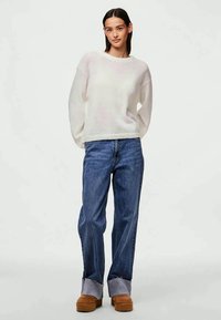 Ελαφρύ, κρεμ πουλόβερ με μακριά μανίκια και χαλαρή εφαρμογή, συνδυασμένο με ίσια μπλε τζιν και χοντρές ταμπά πλατφόρμες.