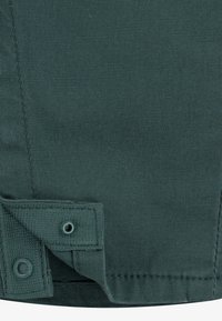 Zelená tkanina s texturovaným povrchem, obsahující záhyb na lemu se zapínáním na cvoček a zesíleným šitím podél okrajů.