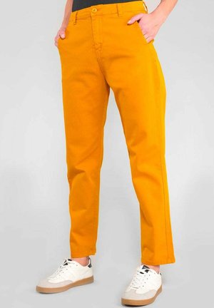 Gelbe Chinos mit schlanker Passform, ausgestattet mit Seitentaschen, einem Knopfverschluss und umgeschlagenen Säumen, kombiniert mit weißen und grauen Sneakern.