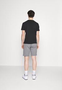 Combinaison d'un t-shirt noir à manches courtes et de shorts gris, en coton, coupe décontractée, modèle portant des baskets blanches et des chaussettes montantes.