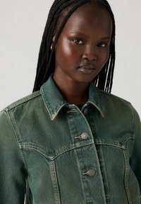 Green denim jacket featuring metal buttons, a classic collar, and a slightly faded texture, designed with chest pockets and a tailored fit.