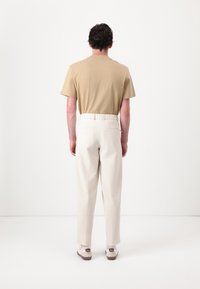 Beige bomulds T-shirt og hvide bukser med elastisk talje, parret med lyse sko, set fra ryggen mod en hvid baggrund.