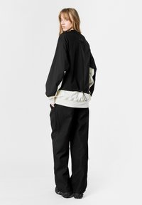 Chaqueta negra con cuello alto, que presenta una sección inferior blanca y un dobladillo con cordón. Combinada con pantalones anchos negros con textura y calzado voluminoso.