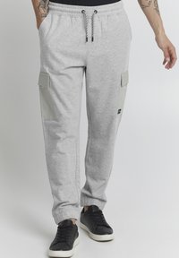Gray sweatpants with cargo pockets, elastic waistband, and drawstring. Soft texture and fitted cuffs, paired with black sneakers.